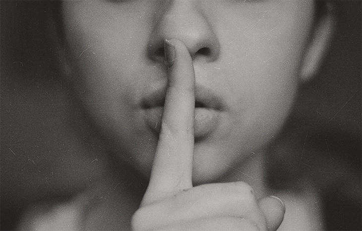 Woman holding her index finger to her lip to signal a secret